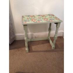 small table chalk painted light green with plastic flowered top edged with pewter nails
