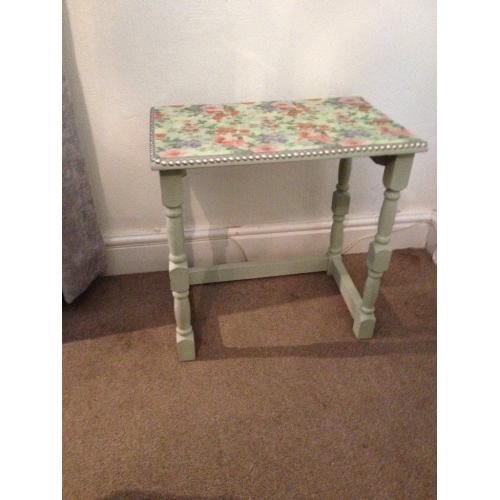 small table chalk painted light green with plastic flowered top edged with pewter nails