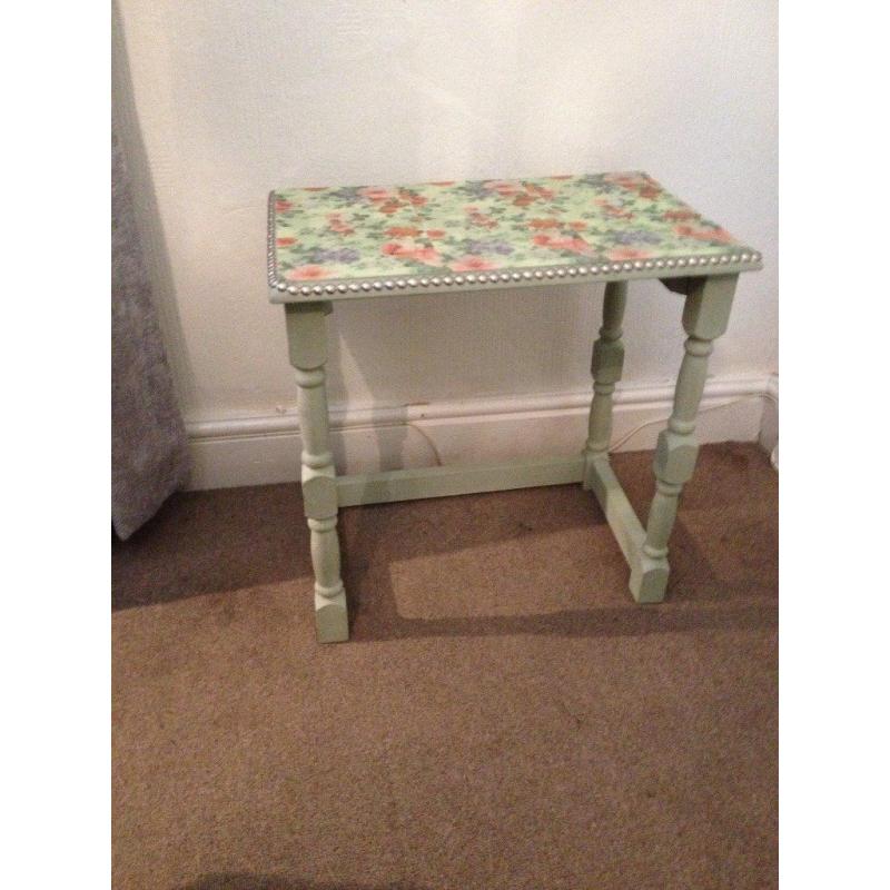 small table chalk painted light green with plastic flowered top edged with pewter nails
